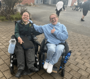 Daisy with a friend, both using wheelchairs and laughing together